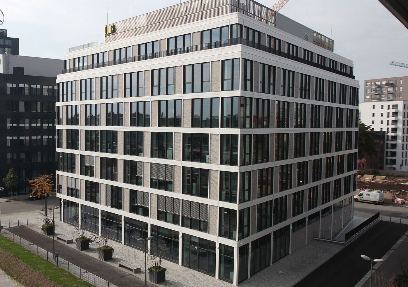 Foto: Sechsstöckiges Bürogebäude mit quadratischem Grundriss und offener Glasfassade, die den Himmel über Berlin spiegelt.